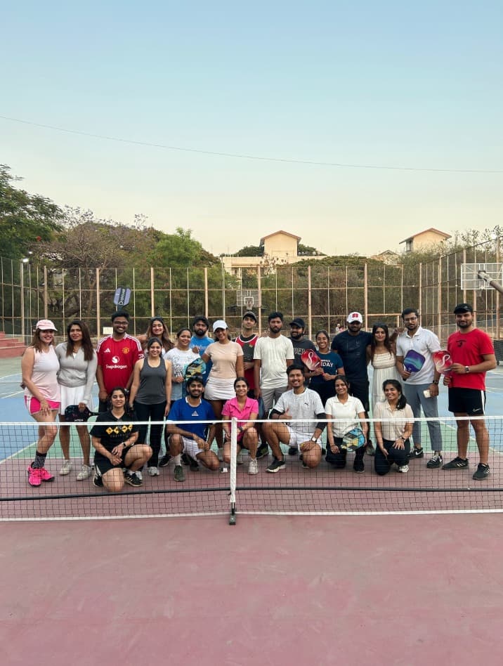 A group of Pickle Haus players holding paddles and smiling around the net on court