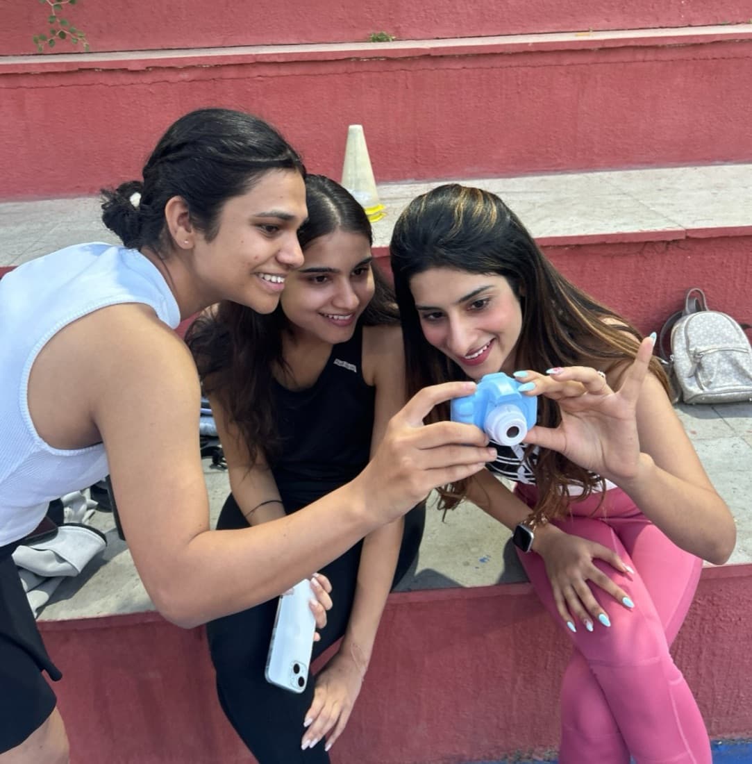 Three friends laughing over a small toy camera on the red courtside steps